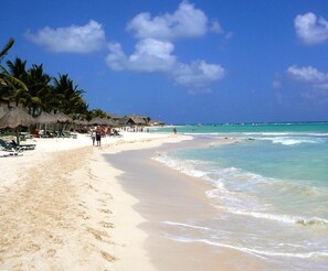 Ein Strand mit strohgedeckten Hütten, Palmen und einem klaren blauen Himmel.