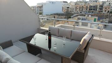 Un balcon avec une table à plateau en verre, des sièges confortables et une bouteille de vin.