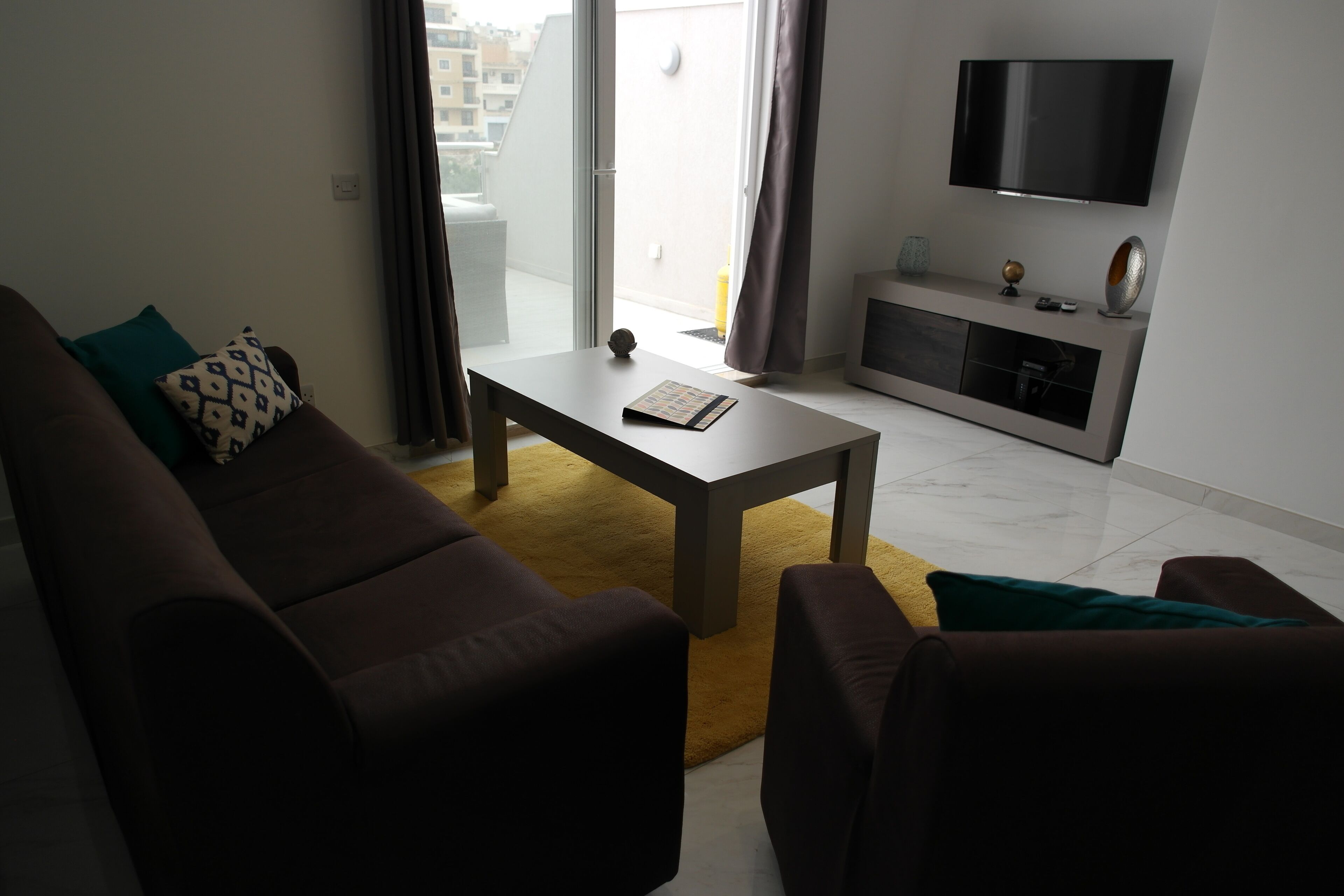 Een moderne woonkamer met een bank, salontafel en een flatscreen televisie aan de muur.