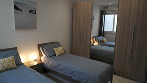 Un dormitorio con dos camas, armarios de madera, una mesita de noche con lámpara y un cuadro en la pared.