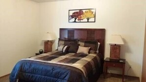 Quarto com cama grande, duas mesas de cabeceira com luminárias, cabeceira e um quadro na parede.