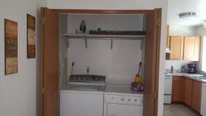 Cozinha compacta com fogão, pia e um pequeno balcão. Há armários acima do balcão e uma porta que dá para outro cômodo.