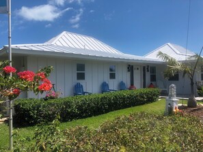 A white house with a metal roof, a front porch with blue chairs, and a well-maintained garden.