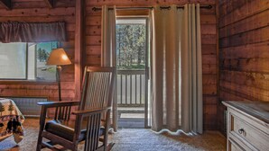 A wooden cabin interior with a wooden rocking chair, a lamp, a view through a window, and a door with curtains. - Stemwinder #3:  3 Bedrooms Plus Bonus Sleeping Loft.  2 Full Baths (Snowshoe)
