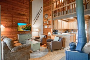 Ein gemütliches Blockhaus-Interieur mit Wohnbereich, inklusive Fernseher, bequemen Sitzgelegenheiten und einem Kaminofen.