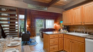 A wooden cabin kitchen with a central island, wooden cabinets, and a dining area with a table set for four. - Stemwinder #3:  3 Bedrooms Plus Bonus Sleeping Loft.  2 Full Baths (Snowshoe)