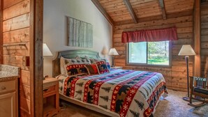 A wooden cabin bedroom with a bed, nightstands, a rocking chair, and a window with a view of the outdoors. - Stemwinder #3:  3 Bedrooms Plus Bonus Sleeping Loft.  2 Full Baths (Snowshoe)