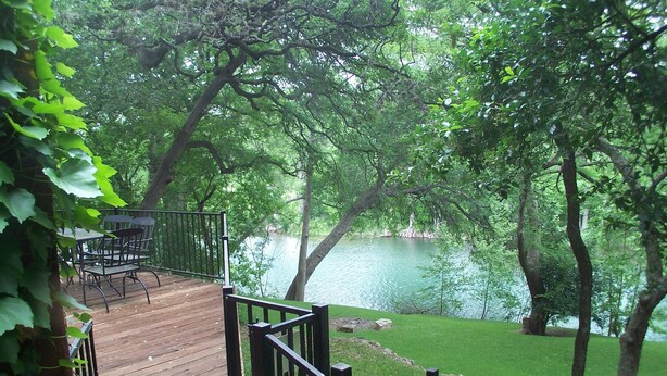 A wooden deck with metal railings overlooking a lake, surrounded by lush greenery.