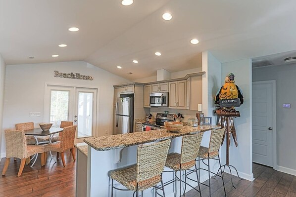 A modern kitchen with a bar area, wicker chairs, and a welcome sign.