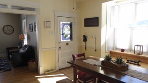 A dining area with a wooden table, chairs, and a bench. There is a door with a glass panel and a sign above it. A coat rack with items hanging is visible on the wall. - Enjoy some R & R at this historic cottage in the best neighborhood in town! (Silverton)