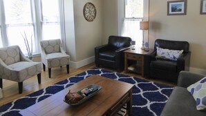 A living room with two armchairs, a sofa, a coffee table, and a lamp. There are windows with curtains, a decorative wall piece, and a rug. - Enjoy some R & R at this historic cottage in the best neighborhood in town! (Silverton)