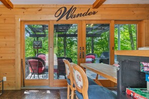 Una cabaña de madera con un letrero que dice 'Wander', una puerta corrediza de vidrio que da a un patio al aire libre con sillas y una mesa.