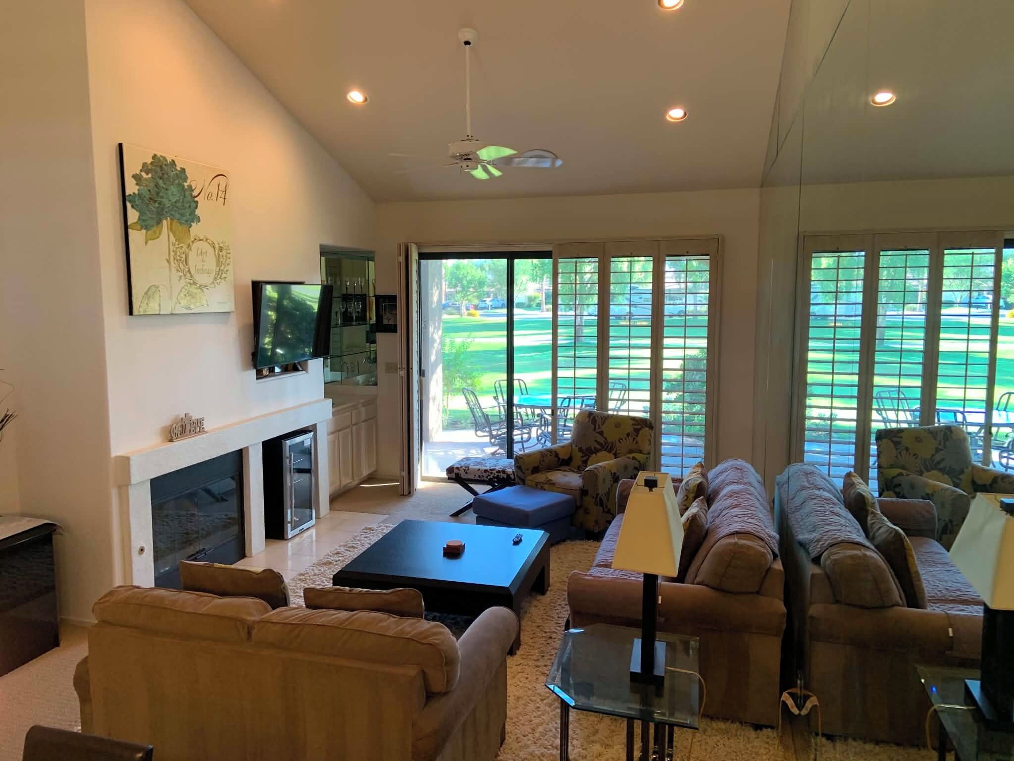 A spacious living room with a fireplace, a television, and a large window overlooking a golf course.