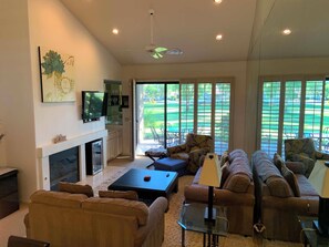 A spacious living room with a fireplace, a television, and a large window overlooking a golf course. - PALM VALLEY COUNTRY CLUB🌴UPDATED2BED+DEN🛋️ 48POOLS💦JAN/FEB OPEN!DISCOUNTED RATES! (Palm Desert)