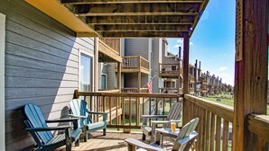 Une terrasse en bois, agrémentée de chaises Adirondack et d’une table, qui offre une vue sur un quartier résidentiel composé de plusieurs immeubles.
