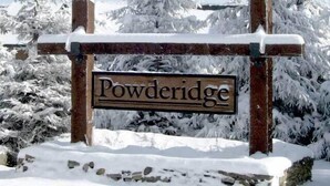 Une pancarte en bois portant le nom « Powderidge », dans un paysage enneigé où les arbres sont recouverts de neige.