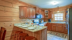 Eine Küche mit Holzausstattung, Granit-Arbeitsplatten, einer zentralen Kochinsel mit Sitzgelegenheiten und einem Kühlschrank.