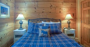 Een kamer met houten lambrisering, een bed, twee bedlampen en een ingelijste foto aan de muur.