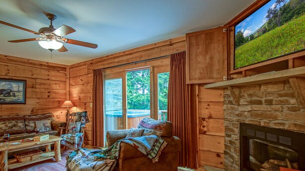 Ein gemütliches Blockhaus-Interieur mit Kamin, Holzwänden, einer Couch, einem Tisch mit Lampe und einem Deckenventilator.