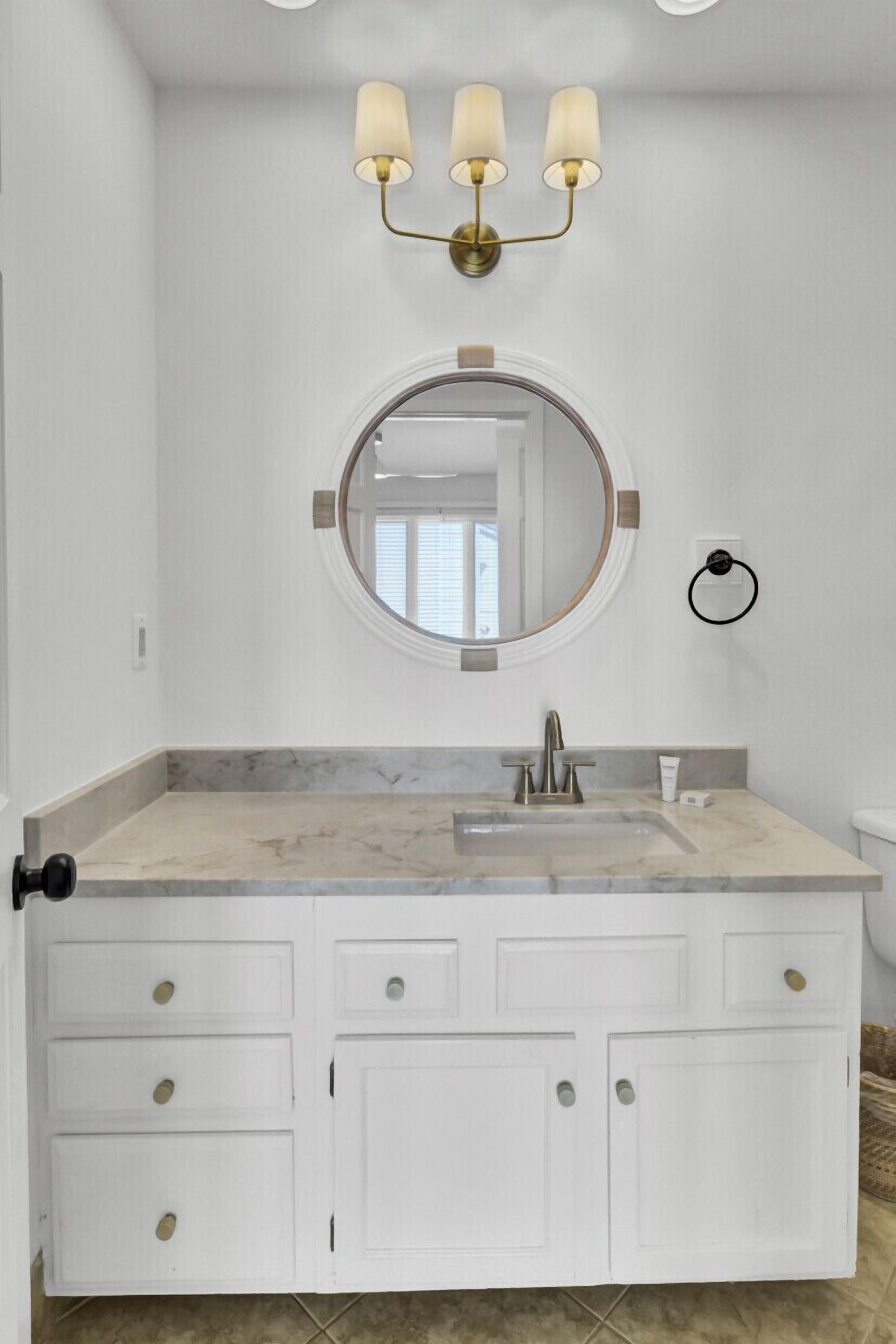 Une salle de bain avec un meuble-lavabo blanc, un miroir rond, un évier et un luminaire fixé au mur.
