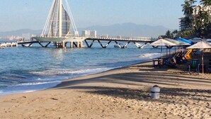 A beach with a bridge, umbrellas, and palm trees. - Zona Romantica Area with Beautiful Bay View and Large Terrace (Puerto Vallarta)
