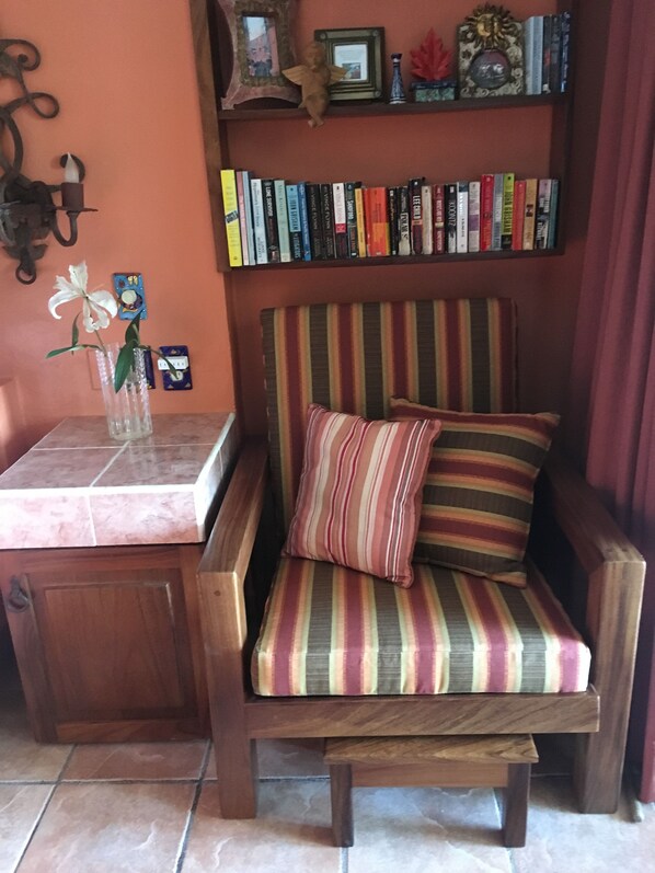 A wooden armchair with a striped cushion, a small table with a vase of flowers, and a bookshelf with various books.