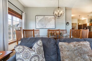 Un comedor con un mapa en la pared, sillas de madera, una araña y vistas a la cocina al fondo.