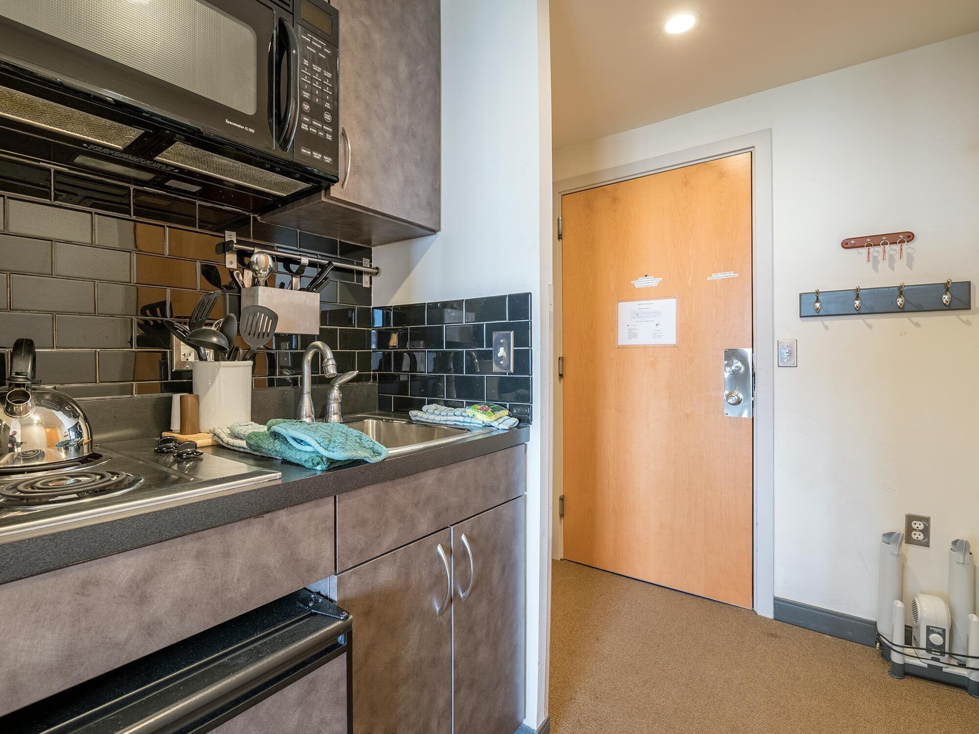 A modern kitchen with a microwave, stove, and sink. There is a wooden door and a coat rack on the wall.