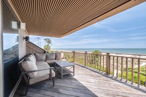 A wooden deck with a cushioned seating area overlooking a beach.