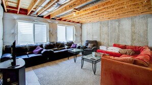 A living room with a high ceiling, exposed wooden beams, a black leather sofa, a red sofa, and a glass coffee table. - Pet Friendly-10 min to Peterson AFB-Pool Table (Colorado Springs)