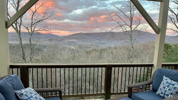 A covered outdoor seating area with wicker furniture and cushions, overlooking a mountainous landscape. - Great location, beautiful mountain and sunset views, hot tub and shuffleboard. (Fairview)