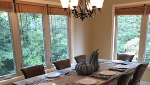A dining room with a large wooden table set for six, surrounded by dark leather chairs. A chandelier hangs above, and the room has large windows with blinds. - Great location, beautiful mountain and sunset views, hot tub and shuffleboard. (Fairview)