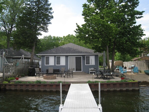 A house with a dock extending into a body of water, surrounded by trees and a fenced yard.