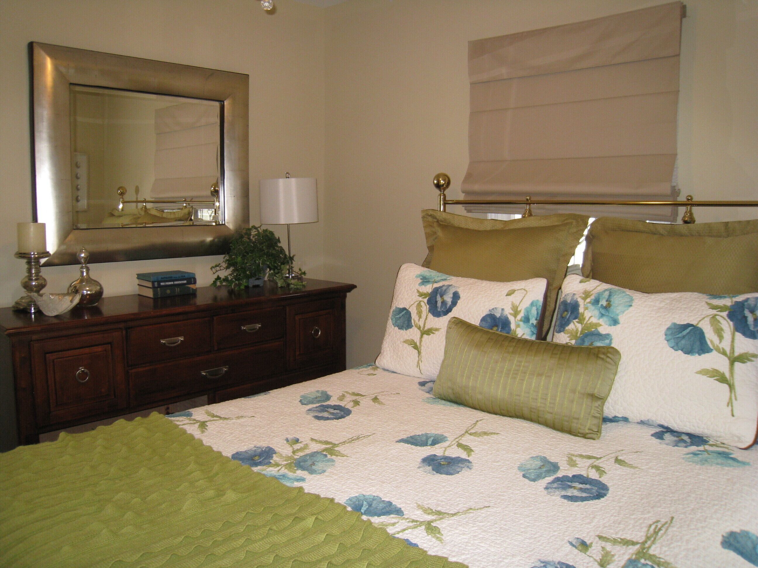 A bedroom with a bed, a dresser, a mirror, and a window with a blind.