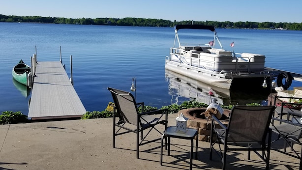 A dock with a green canoe, a boat with an American flag, and outdoor seating with a small table and chairs. - All Sports Lake / Golf, minutes from many players (Lapeer)