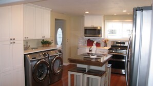 A modern kitchen with stainless steel appliances, a built-in oven, and a microwave. There are wooden stools and a small island with a sink. - All Sports Lake / Golf, minutes from many players (Lapeer)