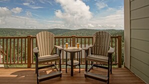 A wooden deck with Adirondack chairs and a small round table, overlooking a forested landscape. - 3 bedroom, 2 Full Baths, Slope Side. Outdoor Hot Tubs on Site. Ski Lift overlook. (Snowshoe)