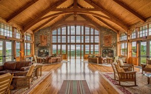 A spacious room with high ceilings and large windows, featuring a fireplace, wooden furniture, and a view of the outdoors. - 3 bedroom, 2 Full Baths, Slope Side. Outdoor Hot Tubs on Site. Ski Lift overlook. (Snowshoe)