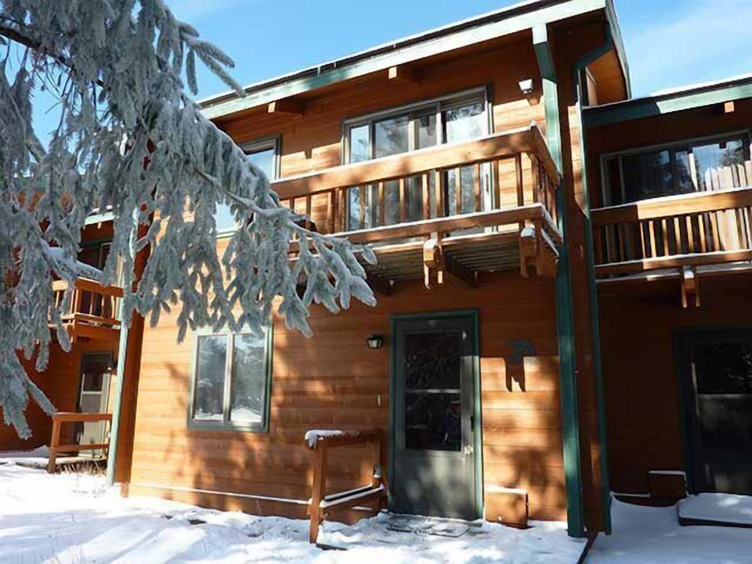 A wooden cabin with a balcony, a door, and windows.