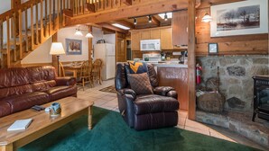 Un intérieur de chalet chaleureux avec un escalier en bois, des canapés en cuir, un coin repas et une cuisine.