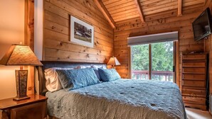 Une chambre de style cabane en bois, avec un lit, deux lampes de chevet, une commode et un téléviseur fixé au mur.