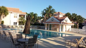 Una piscina con sillas de descanso y sombrillas, rodeada de palmeras y un edificio con tejado de baldosas.