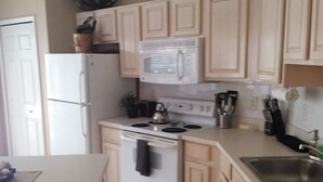 Una cocina con alacenas de colores claros, un refrigerador blanco, un microondas, una estufa y un lavaplatos.