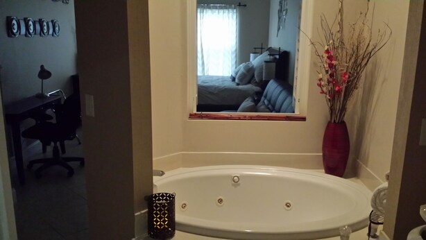 Un baño con una bañera grande, un espejo, un inodoro y un escritorio con una silla.