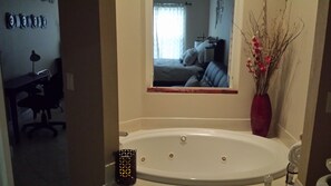 A bathroom with a large bathtub, a mirror, a toilet, and a desk with a chair.
