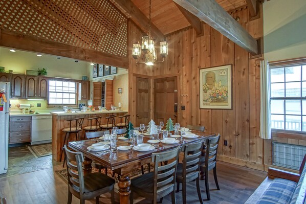 Un intérieur en bois comprenant un coin repas aménagé pour six personnes, une cuisine avec des meubles en bois et une grande fenêtre.