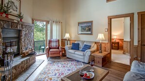 A cozy living room with a fireplace, a sofa, a coffee table with wine glasses, and a view of the outdoors. - Whistlepunk #24: 4 Bedroom, 3 Bath:  Slope Side, Wood Fireplace. (Snowshoe)