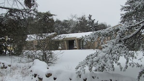 Un edificio rustico con facciata in pietra, circondato da alberi innevati e un muro di pietra.