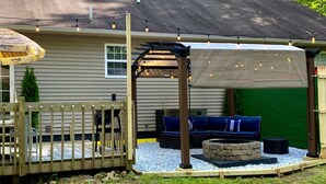 A backyard with a wooden deck, outdoor seating, a fire pit, and string lights. - Urban Edition (Long Pond)