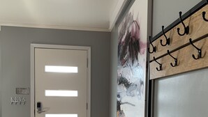 A hallway with a wooden bench, a door with frosted glass panels, a wall-mounted art piece, and a coat rack. - Urban Edition (Long Pond)